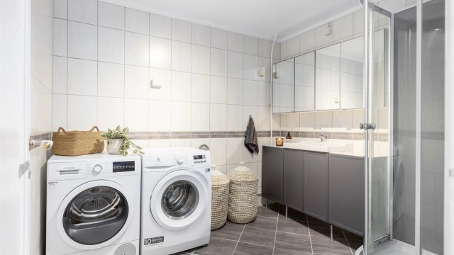 Kombinert baderom og vaskerom med flislagte overflater, gulvvarme og opplegg for vaskemaskin.