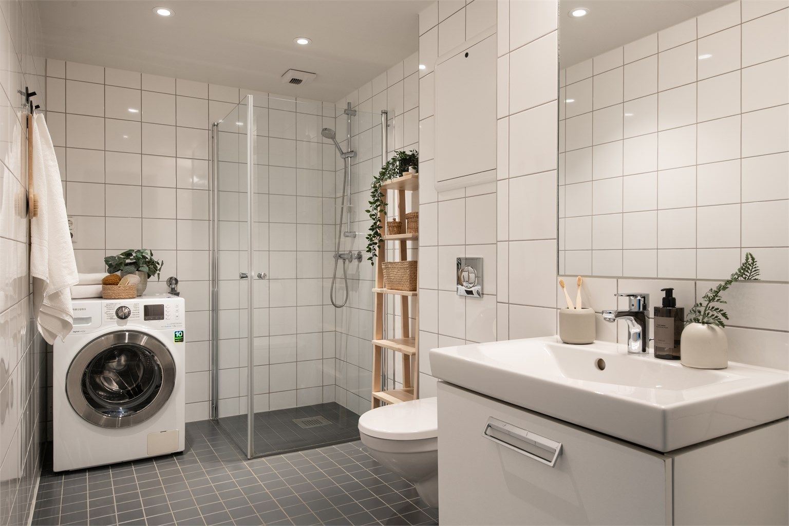 Delikat og flislagt bad med varme i gulv, himling med downlights, vegghengt servant med glatte fronter og ovenpåliggende servant med ett-greps armatur, samt vegghengt speil med belysning og stikkkontakt.