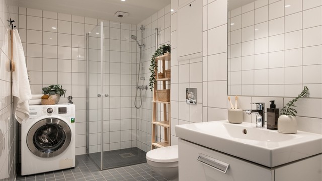 Delikat og flislagt bad med varme i gulv, himling med downlights, vegghengt servant med glatte fronter og ovenpåliggende servant med ett-greps armatur, samt vegghengt speil med belysning og stikkkontakt.