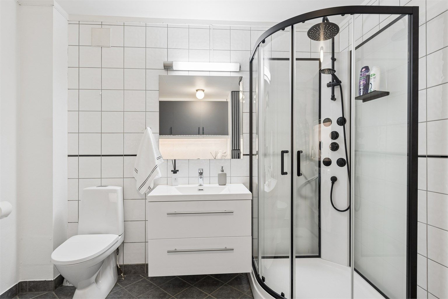 Badet har flislagt gulv med gulvvarme, fliser på veggene og innredning med servant, speil og høyskap.
