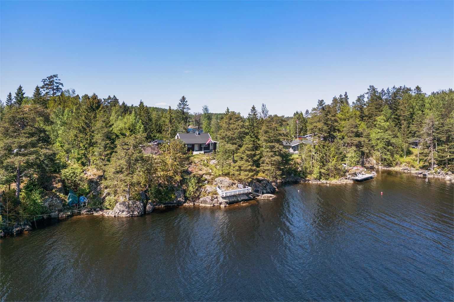 Tomten er noe kupert/plan, opparbeidet med plen, flaggstang, beplantning og noe fjell opp i dagen