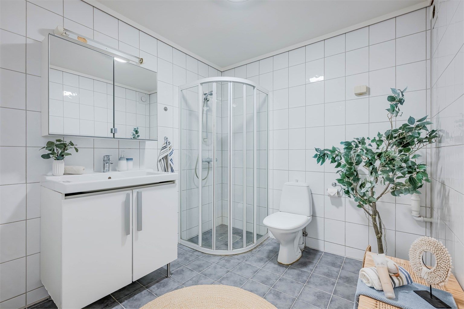 Helfliset romslig bad fra ukjent årstall som er innredet med baderomsmøbler, speilskap, dusjhjørne med dører og gulvstående toalett. Her er også opplegg for vaskemaskin.