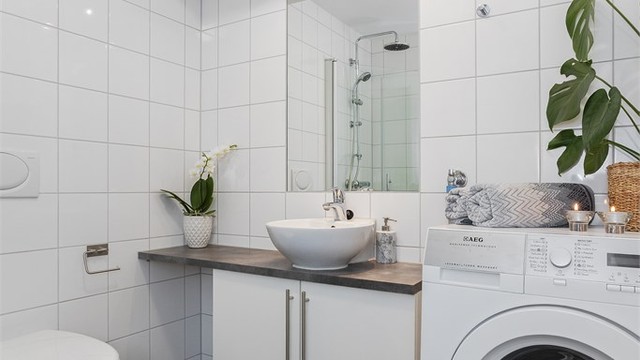 Baderomsinnredningen har ovenpåliggende servant, speil med belysning og opplegg for vaskemaskin.