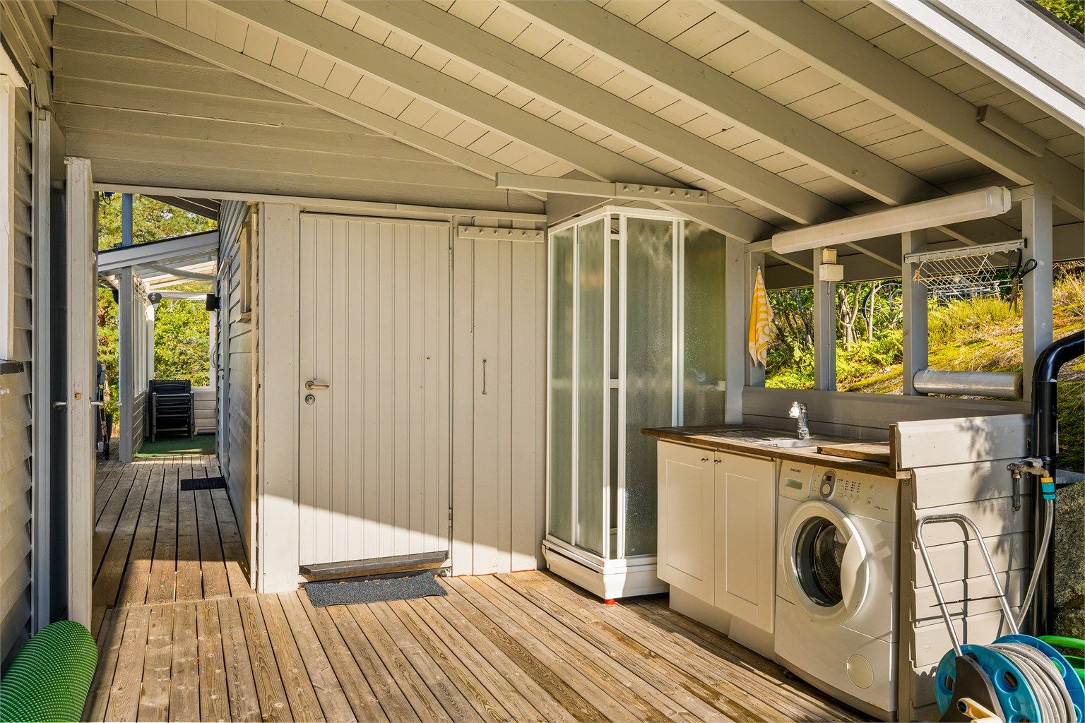 Utekjøkken, vaskemaskin og dusjkabinett under tak.