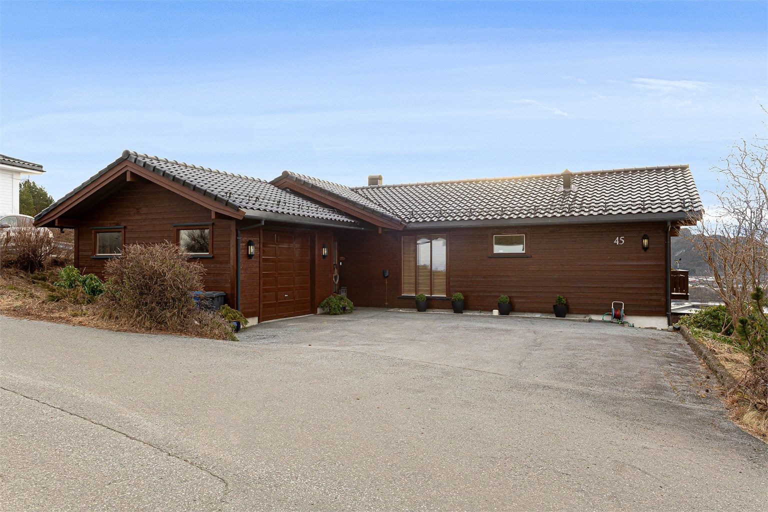 Fasade mot nord med asfaltert gårdsplass, garasje og inngangsparti 