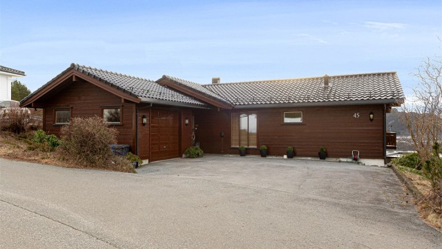 Fasade mot nord med asfaltert gårdsplass, garasje og inngangsparti