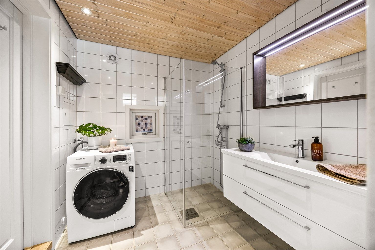 Baderom med flislagte overflater, gulvvarme, dusjhjørne og opplegg for vaskemaskin.