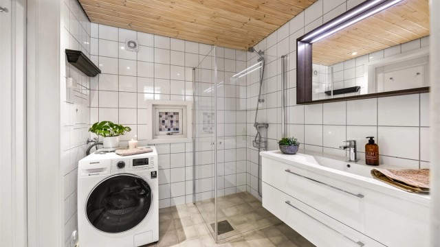 Baderom med flislagte overflater, gulvvarme, dusjhjørne og opplegg for vaskemaskin.