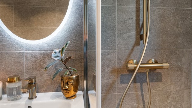 Badet har et dusjhjørne med glassdør og to-greps armatur tilkoblet hånddusj, samt gulvstående toalett