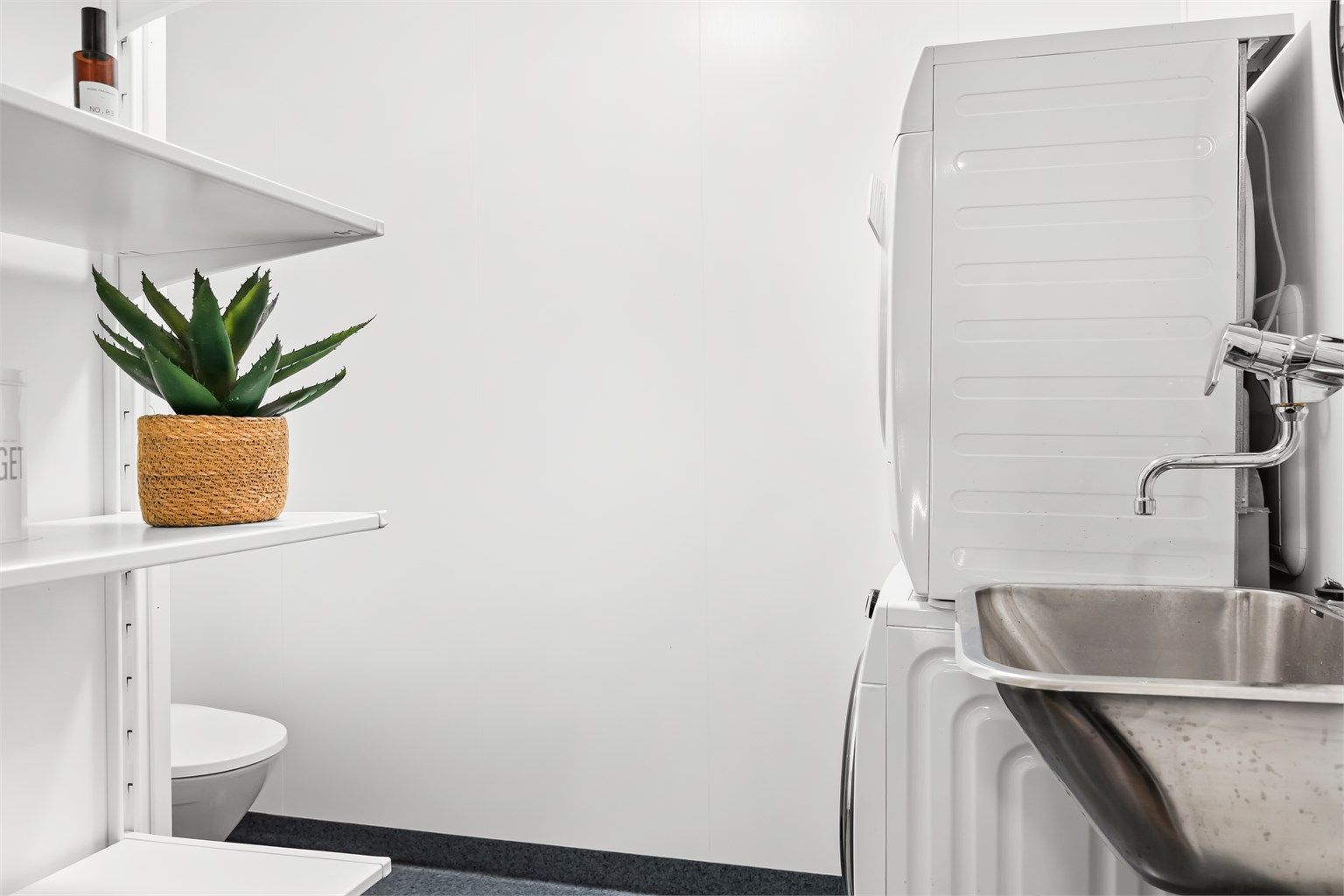 Praktisk vaskerom med gulvmontert toalett, utslagsvask og opplegg for vaskemaskin.