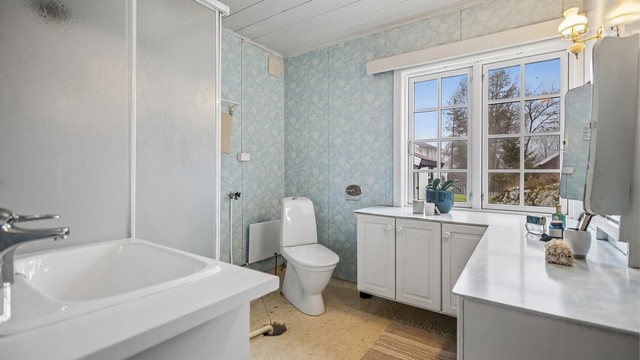 Eldre bad med dusjkabinett, servantinnredning, gulvstående toalett og opplegg for vaskemaskin.
