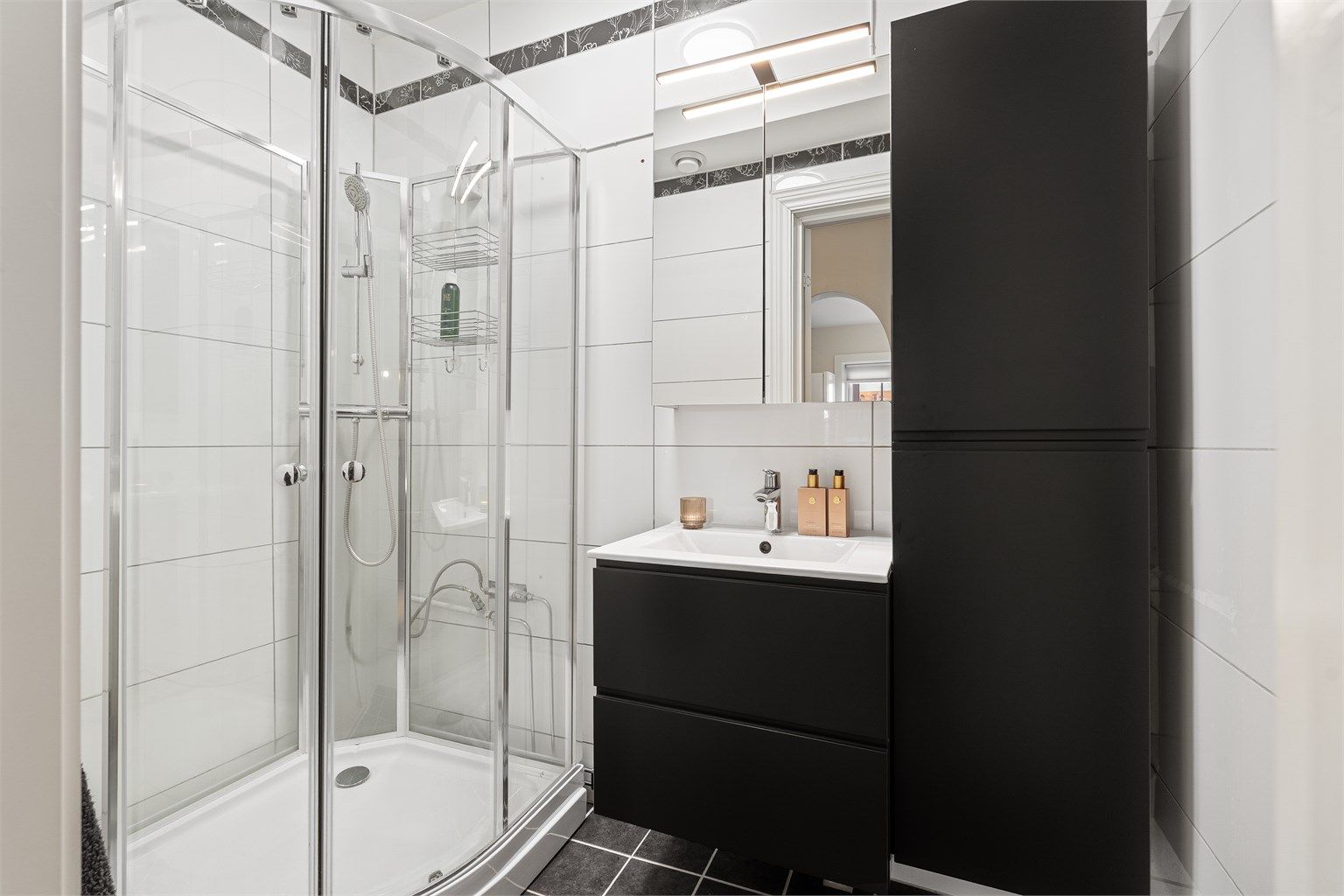 Pent, flislagt bad fra ca. 2010 med dusjkabinett og moderne baderomsinnredning fra 2023, samt et speilskap for ekstra oppbevaring. 