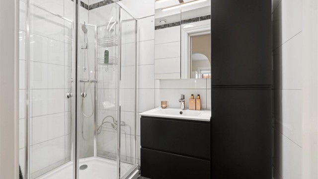 Pent, flislagt bad fra ca. 2010 med dusjkabinett og moderne baderomsinnredning fra 2023, samt et speilskap for ekstra oppbevaring.