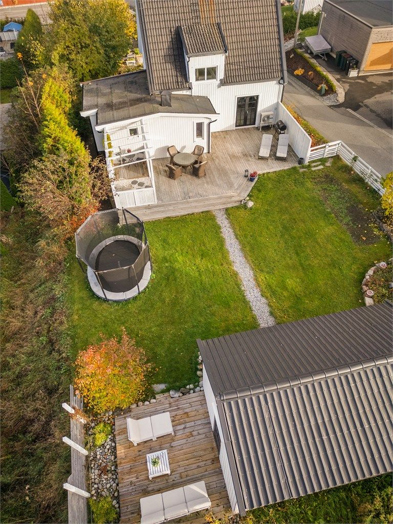 Svakt skrånende tomt som er pent opparbeidet med gressplen, trær, gjerde, hekk, prydbusker og diverse beplantninger.