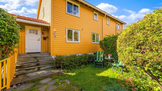 Frodig hage med opparbeidet plen, prydbusker og hyggelig sitteplass foran inngangen.