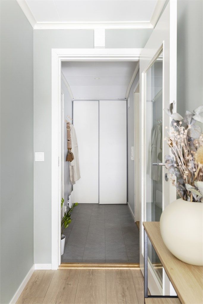 Man kommer inn i en flislagt entré med gulvvarme, skyvedørsgarderobe og knaggrekke.