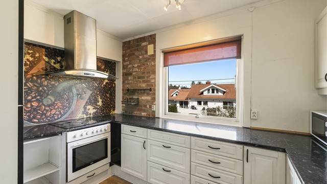 Kjøkkenet ligger i eget rom og har kjøkkeninnredning med profilerte fronter og laminert benkeplate. Det er fliser mellom overskap og benkeplate.