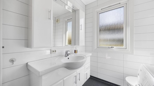 Baderomsinnredning med heldekkende servant, speil med overlys og et praktisk vegghengt skap.