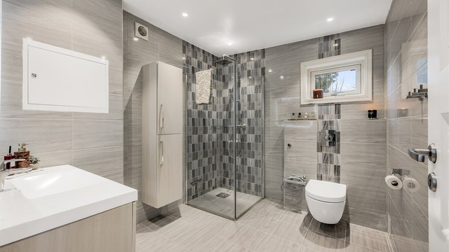 Rommet har vegghengt servantinnredning, speil med integrert lys og et dusjhjørne med innfellbare dører.