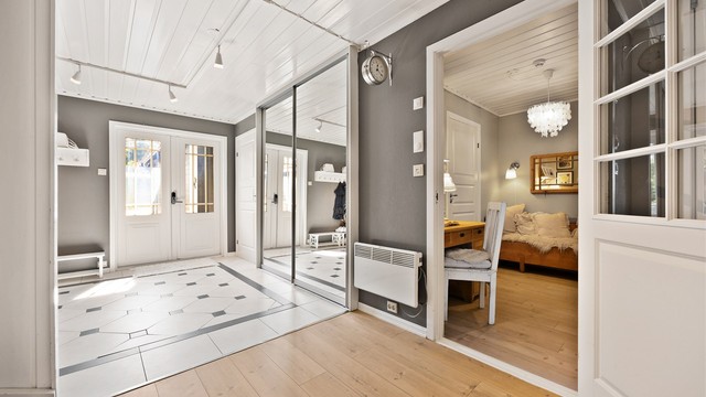 Romslig hall i underetasjen med flislagt gulv og skyvedørsgarderobe.