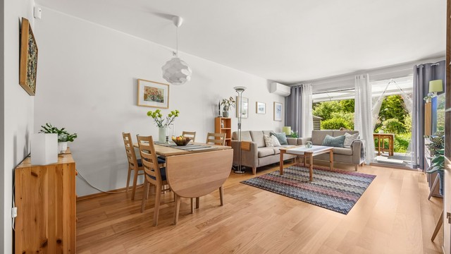 Lys og romslig stue med god plass til både spisebord og sittegruppe, varmepumpe fra 2023 og direkte utgang til den solrike terrassen. Foto: Martine Eren Jacobsen