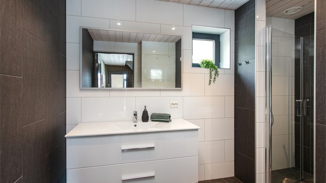 Flislagt bad i 1. etasje med gulvvarme, hvit baderomsinnredning og dusjhjørne.