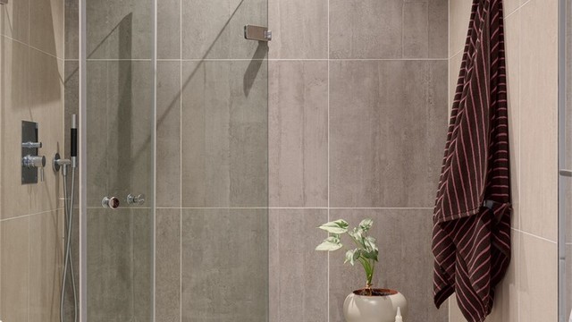 Dusjhjørne med innfellbare glassdører og regndusj. I himlingen er det integrerte høyttalere og i gulvet er det varmekabler.