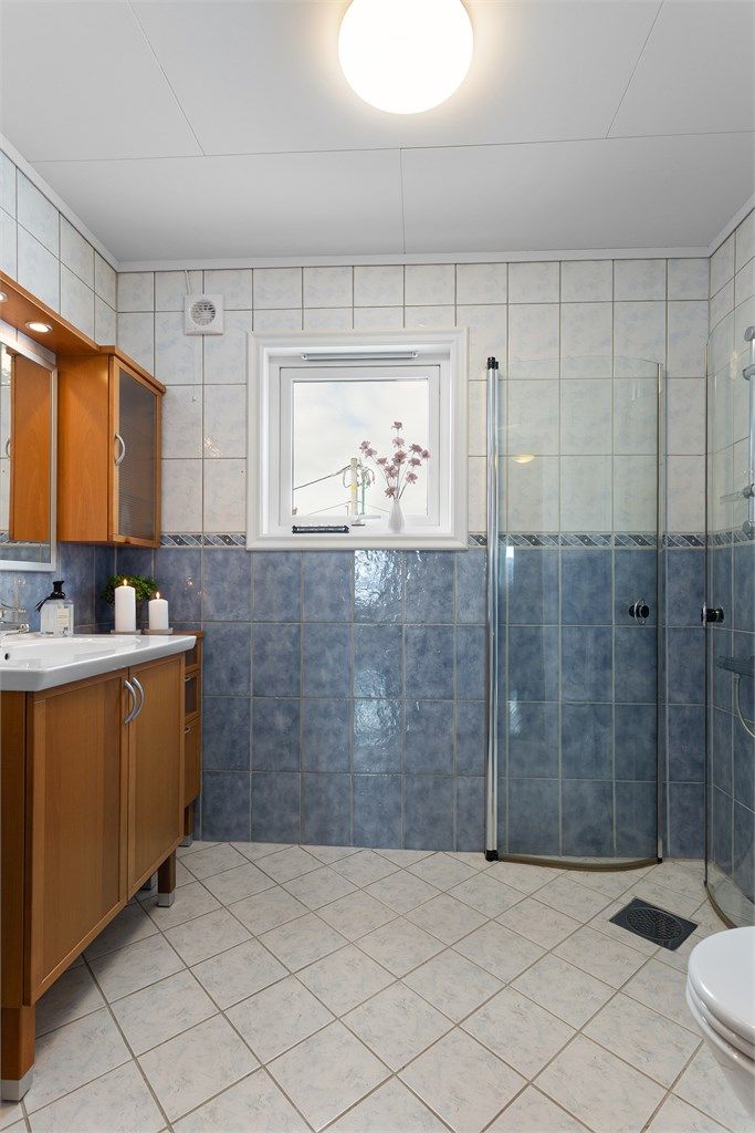 Flislagt bad i hybelen med gulvvarme. Innredning med glatte fronter og vitrineskap.