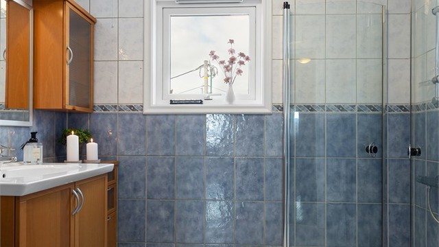 Flislagt bad i hybelen med gulvvarme. Innredning med glatte fronter og vitrineskap.