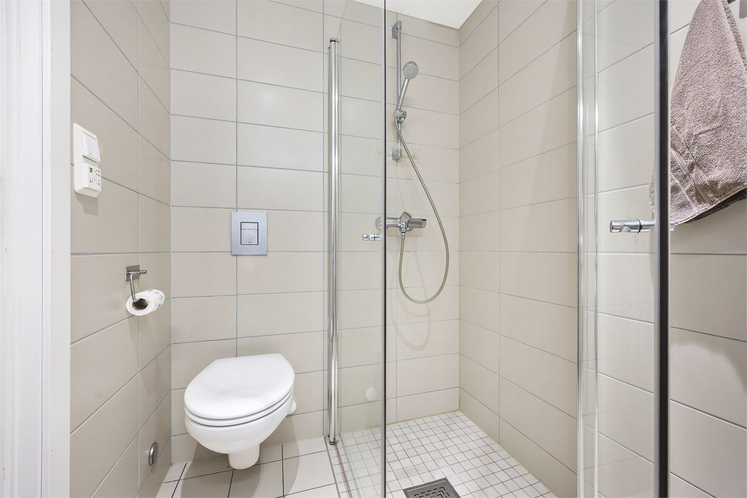 Badet er utstyrt med vegghengt toalett og et dusjhjørne med innfellbare glassdører.