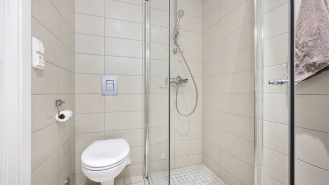 Badet er utstyrt med vegghengt toalett og et dusjhjørne med innfellbare glassdører.