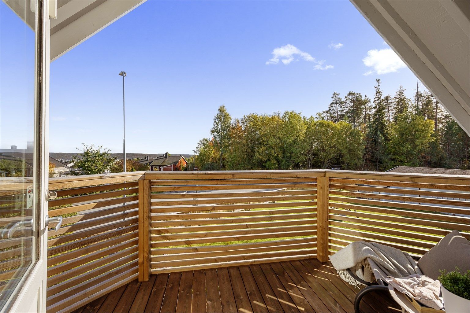Overbygd balkong i trekonstruksjon med terrassebord og spilerekkverk.