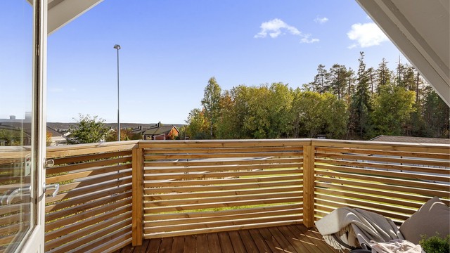 Overbygd balkong i trekonstruksjon med terrassebord og spilerekkverk.