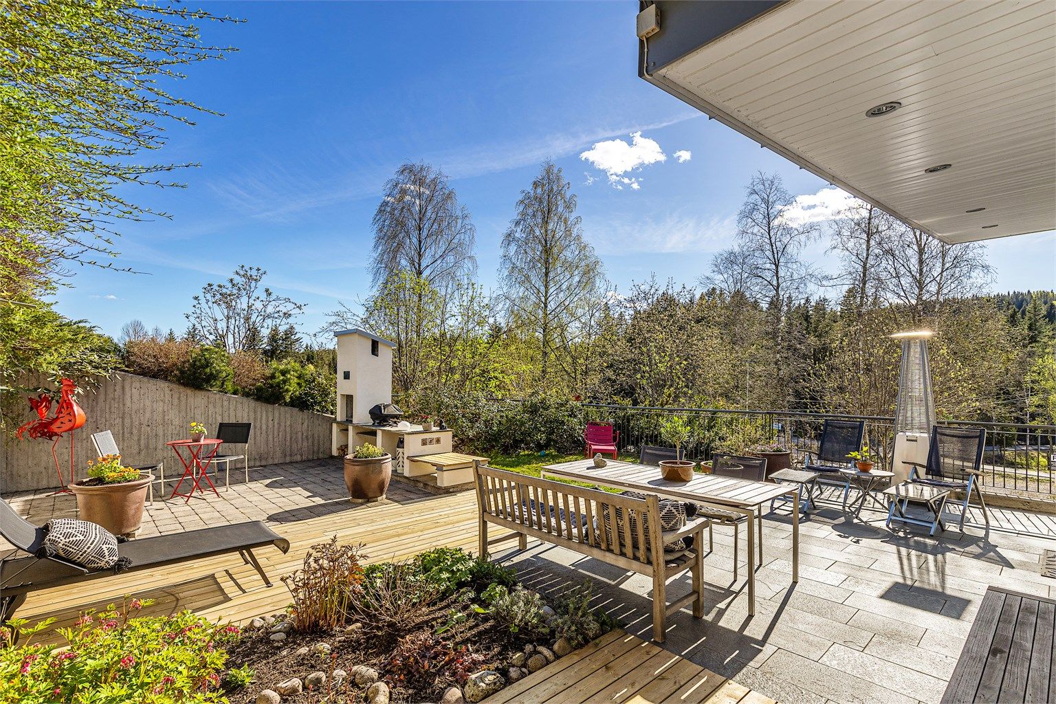 Uteplassen er stilig opparbeidet med både flissatt terrasse og markterrasse i tre. Fin hellelagt plass ved utepeisen. Solid forstøtningsmur i betong. Små grønne lunger innskutt i plassen