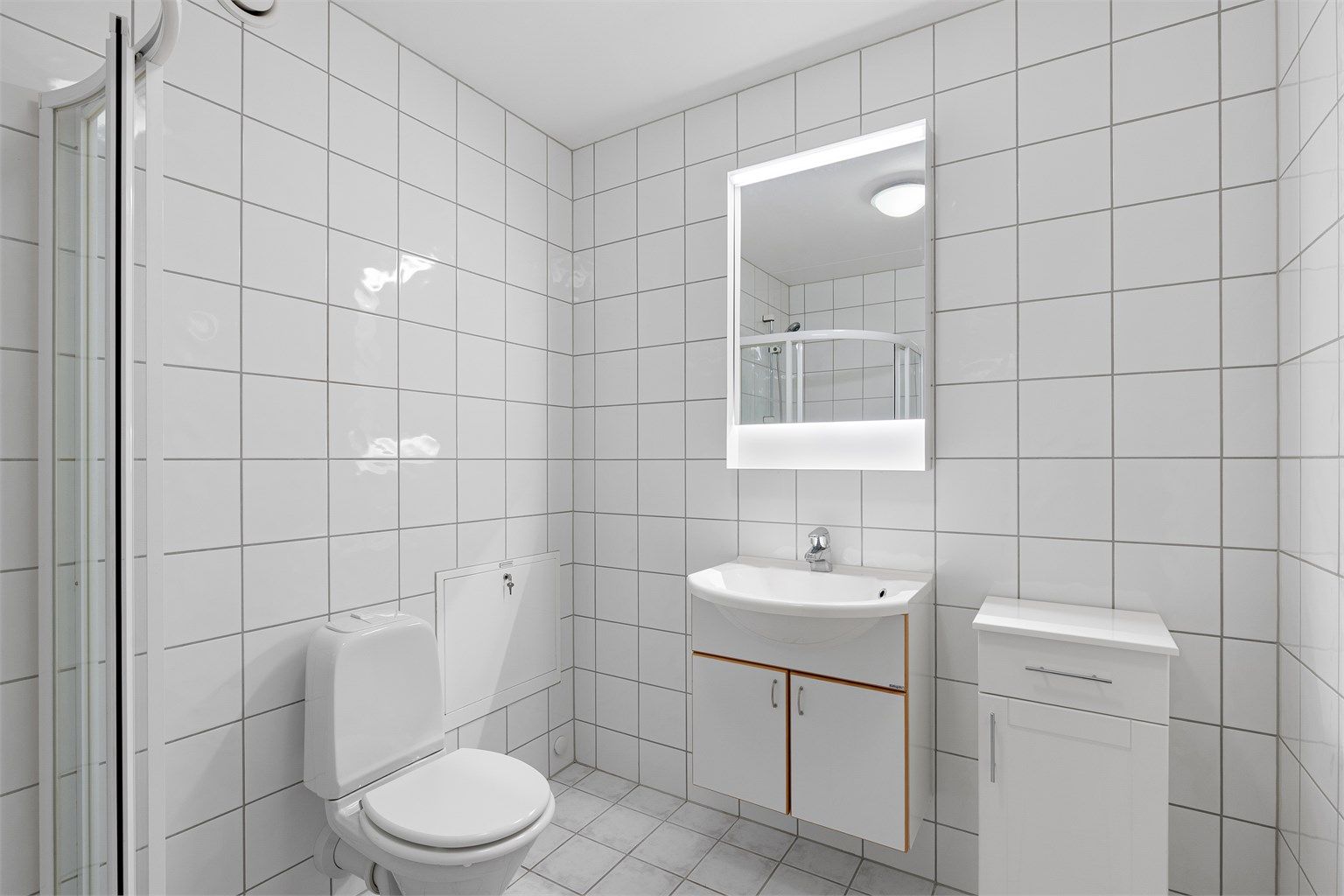 Badet er innredet med dusjhjørne, vegghengt servant med speil