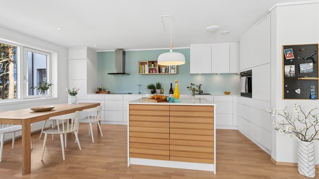 Kjøkkenet har et moderne og stilrent uttrykk, hvor store vindusflater og harmoniske fargevalg skaper en naturlig forbindelse til omgivelsene utenfor.