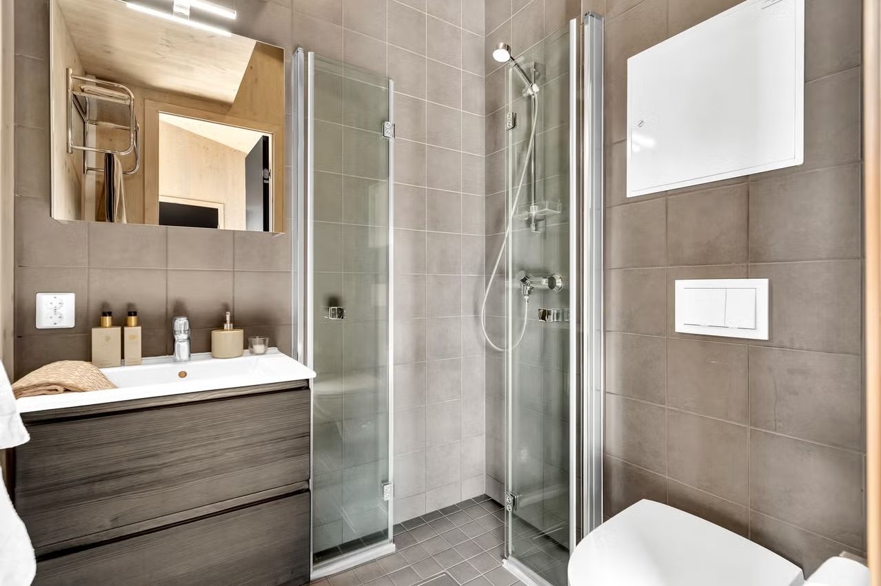 Badet er bestående av flislagt gulv med varme, dusjhjørne med foldbare dører og vegghengt toalett.