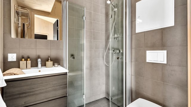 Badet er bestående av flislagt gulv med varme, dusjhjørne med foldbare dører og vegghengt toalett.