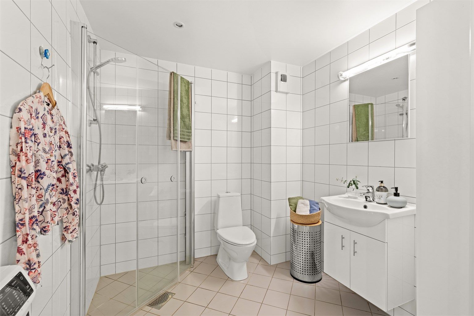 Badet er helfliset og utstyrt med elektriske varmekabler i gulvet, dusjhjørne og servant med underskap.