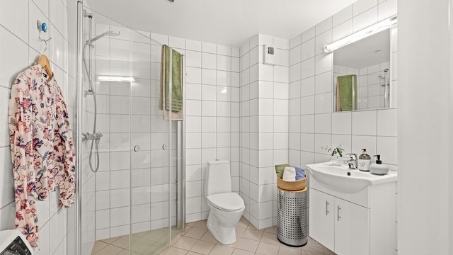 Badet er helfliset og utstyrt med elektriske varmekabler i gulvet, dusjhjørne og servant med underskap.