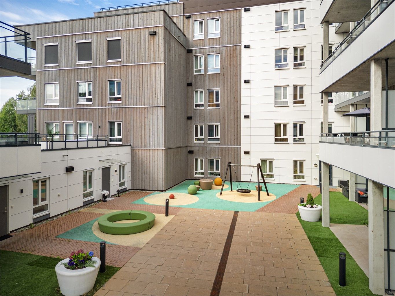 Felles bakgård med hellelagte områder, sitteplasser, lekeapparater og diverse beplantning