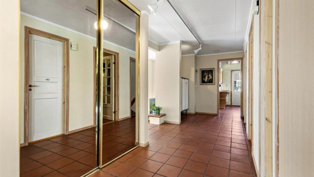 Boligens entré har god plass til oppbevaring av yttertøy og sko. Hallen er romslig med skyvedørsgarderobe. Fra hallen kommer man til kontor, begge stuene og kjøkken, samt trappegang opp til annen etasje og ned til kjeller