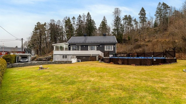 FRODIG HAGEROM MED grønn gressplen, blomsterbed og hekk mot gata.