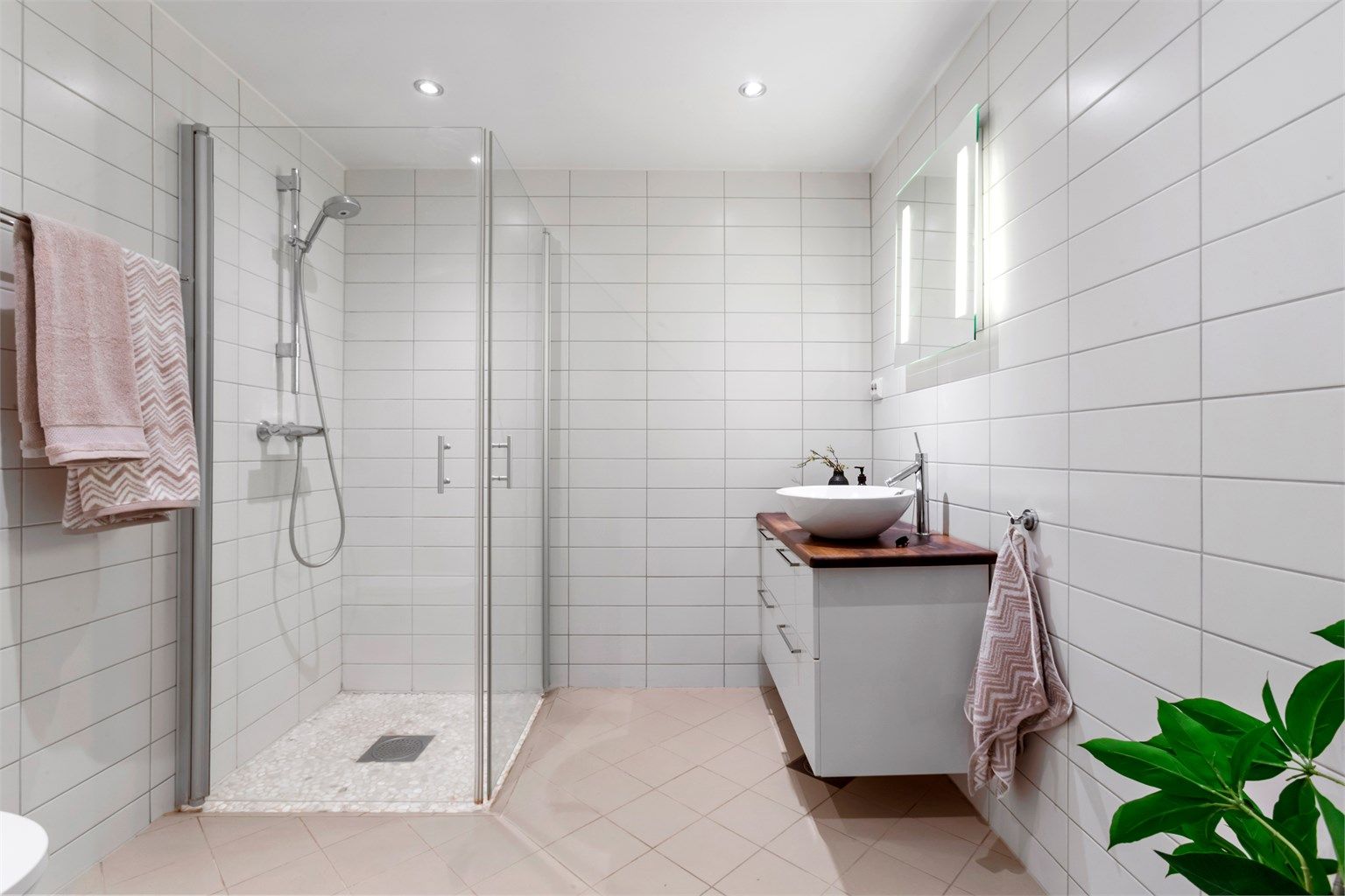 Flislagt bad med gulvvarme, dusjhjørne med innfellbare glassdører og downlights i taket.