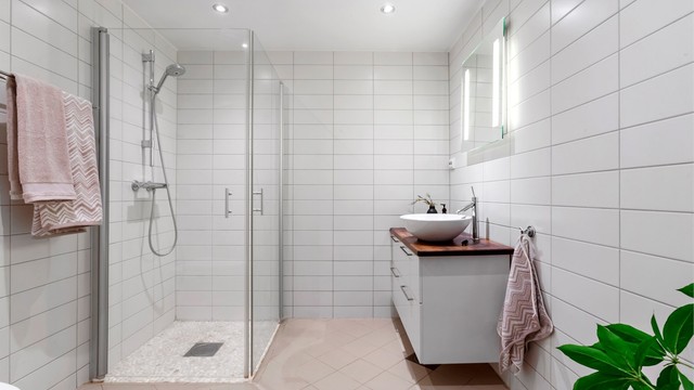 Flislagt bad med gulvvarme, dusjhjørne med innfellbare glassdører og downlights i taket.