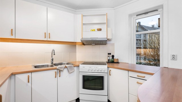 Kjøkkenet er fra ukjent årstall med glatte fronter og benkeplate av laminat. Mellom kjøkkenbenk og overskap er det fliser.