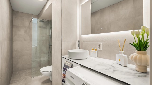 Lekkert, flislagt bad med gulvvarme fra 2025. Badet er innredet med vegghengt toalett, dusjhjørne med glassvegg og opplegg for vaskemaskin.