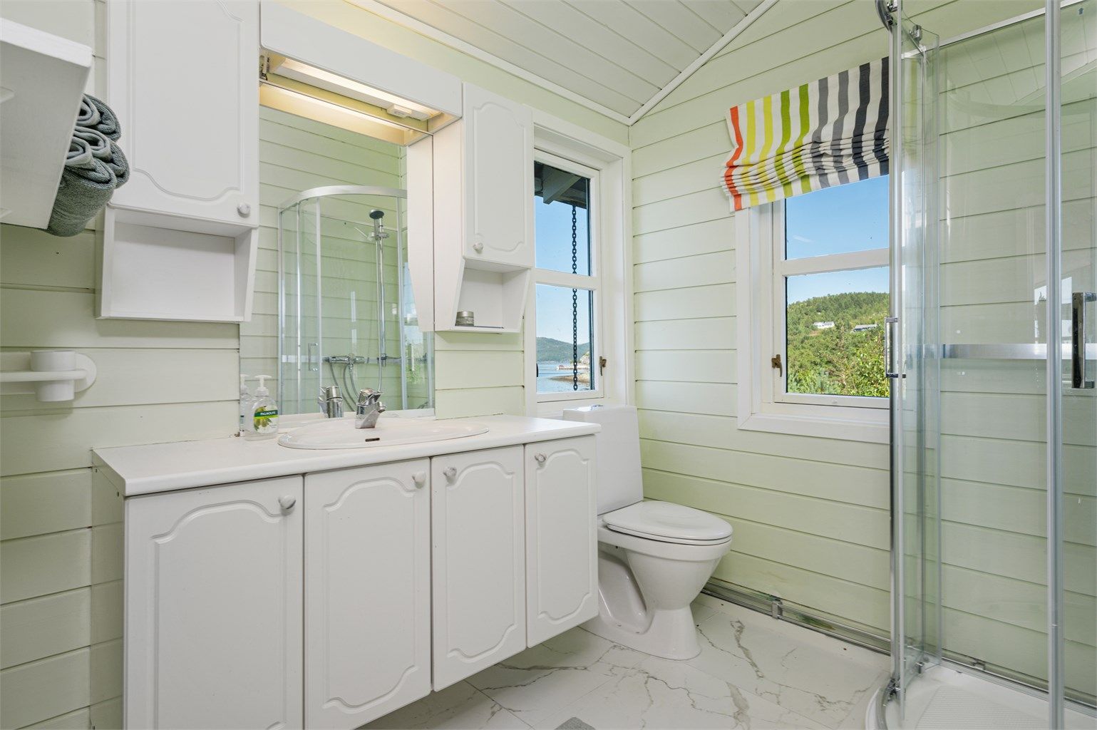 Badet er pent innredet med servantskap med overskap og speil med lys, toalett og dusjkabinett. 