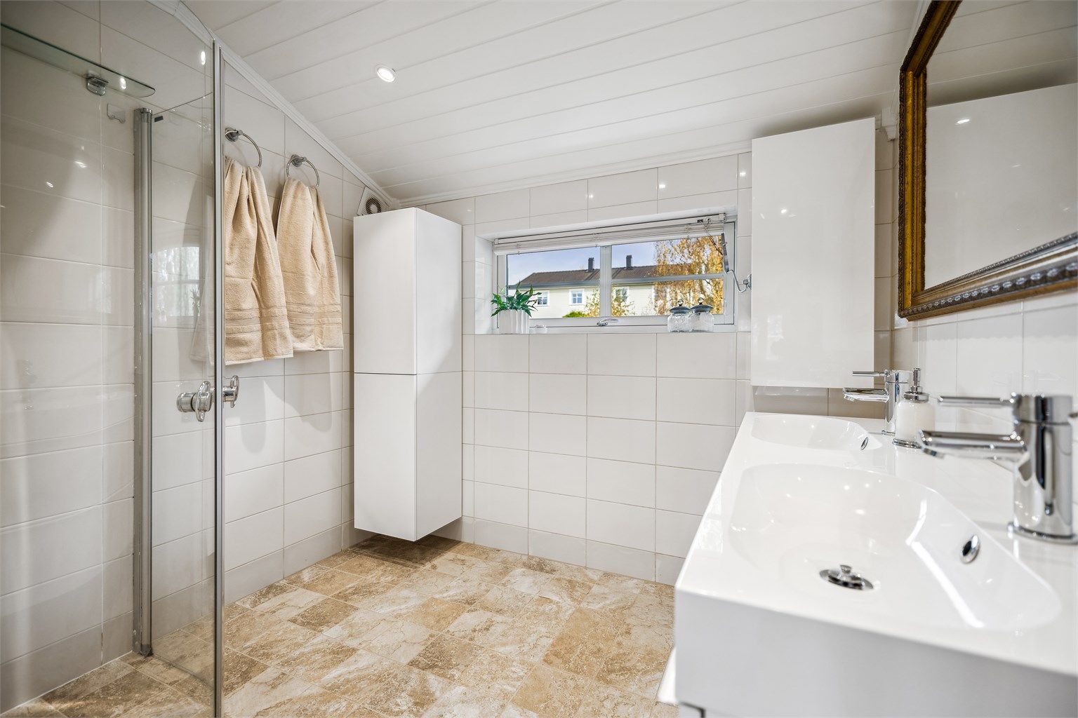 Delikat, flislagt bad med gulvvarme, baderomsinnredning med to servanter og veggskap med glatte fronter i høyglanset utførelse