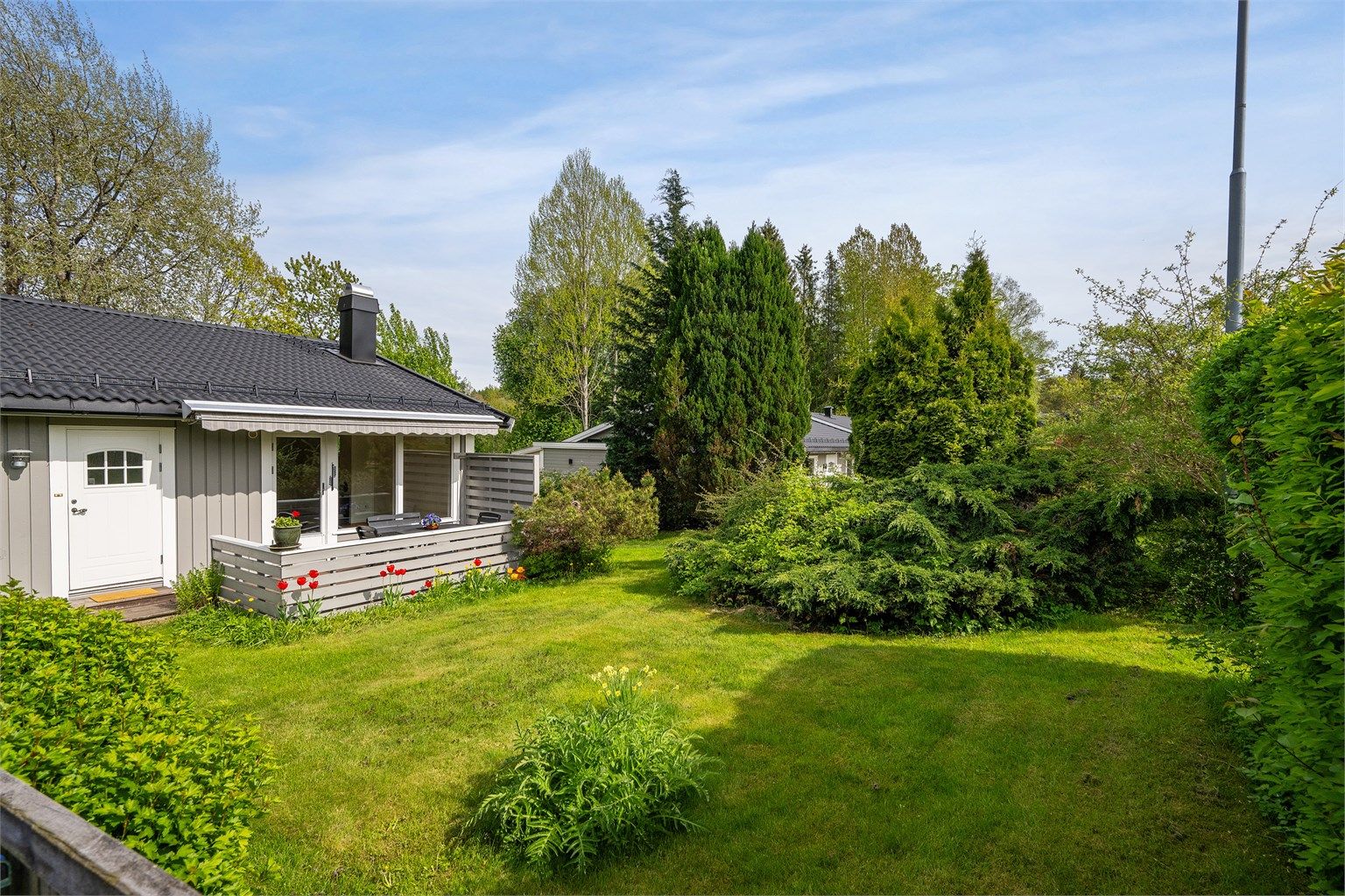 Solrik hage som er hyggelig opparbeidet med gressplen, blomser og diverse beplantning av busker. 